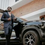 An Indian groom poses elegantly in front of a modern residence, exuding confidence.