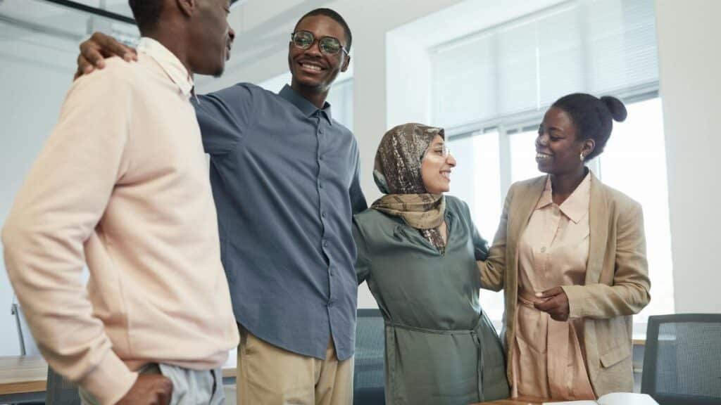 A diverse group of colleagues in corporate attire smiling and embracing in an office setting.