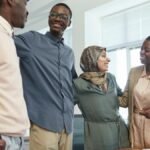 A diverse group of colleagues in corporate attire smiling and embracing in an office setting.