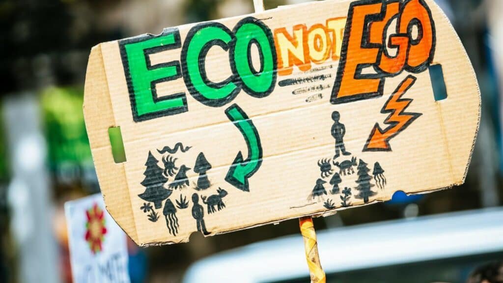 Close-up of a cardboard protest sign with 'Eco Not Ego' message at a climate rally.
