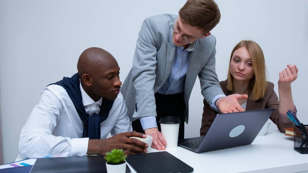 Three professionals engage in a lively business discussion at a modern office desk, focusing on teamwork.