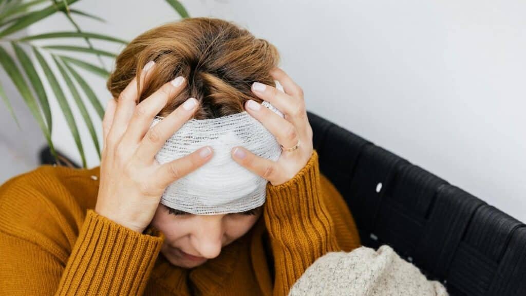 Woman with head injury holding her head in pain indoors.