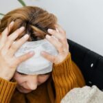 Woman with head injury holding her head in pain indoors.