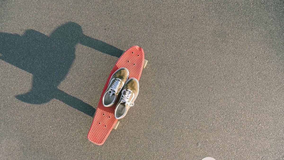 Overhead shot of sneakers placed on a skateboard casting a shadow on asphalt ground.