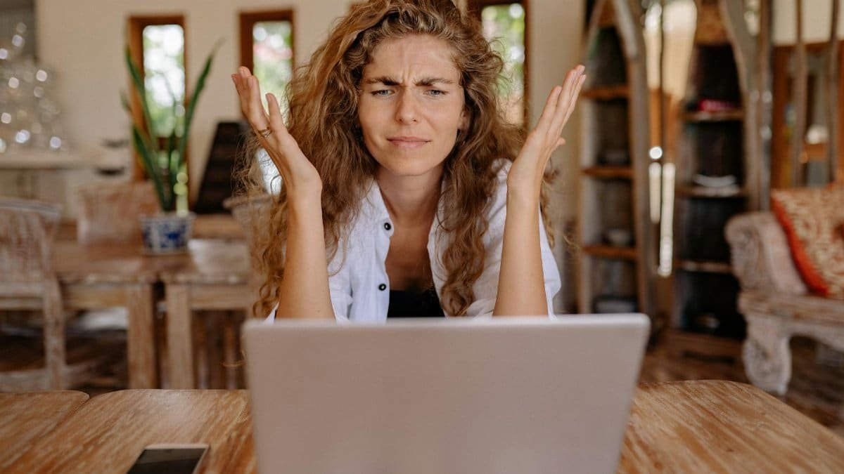 A woman frustrated with her laptop while working remotely indoors, expressing stress.