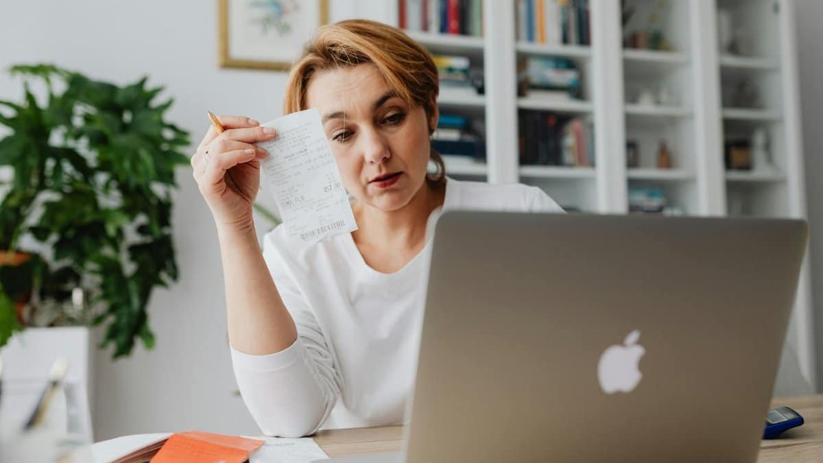 Woman concentrating on receipts while using a laptop, reflecting financial stress.