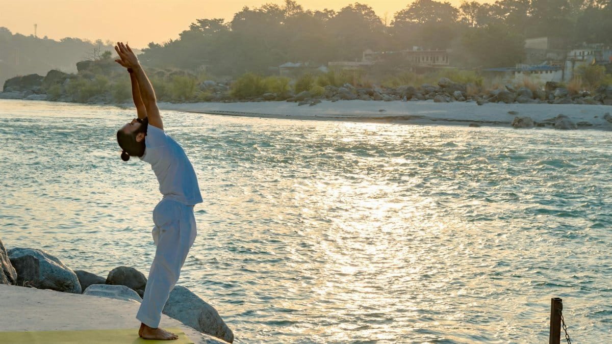 A man performs yoga by the Ganges River in Rishikesh at sunrise, embracing tranquility and mindfulness.