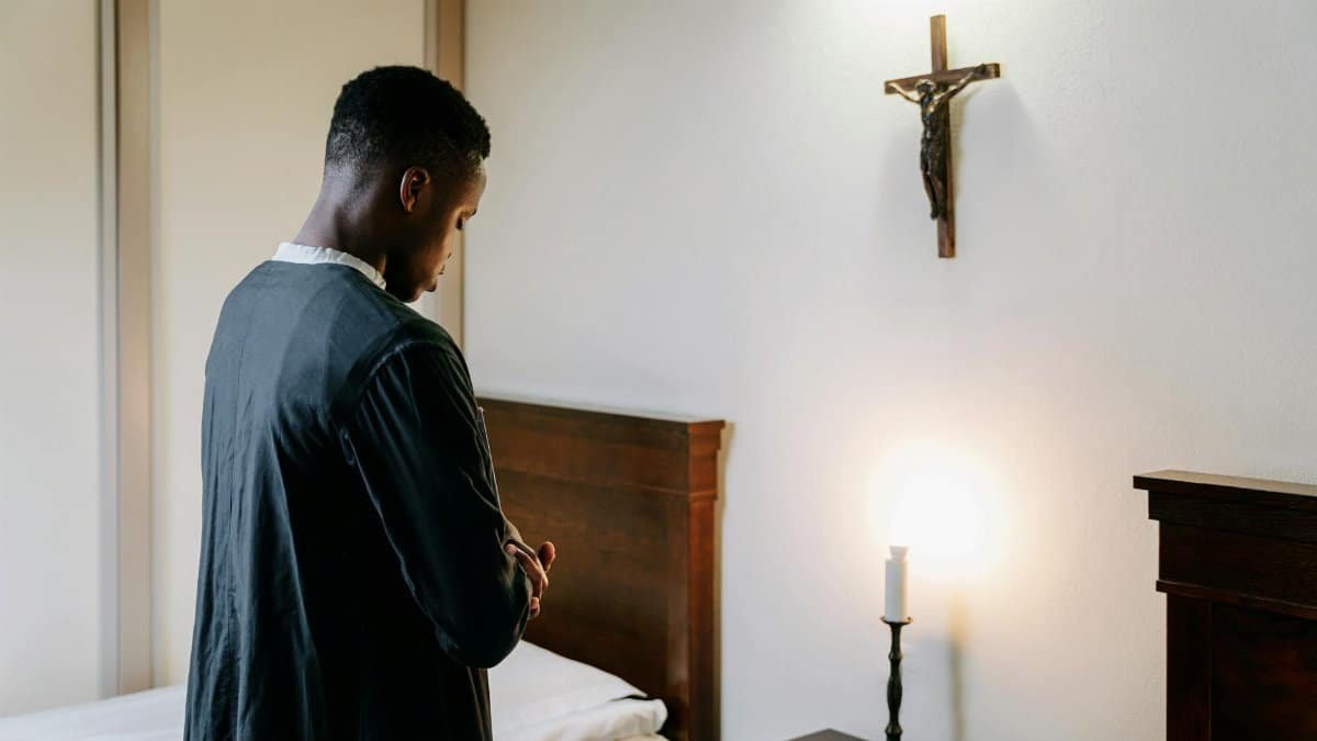 A man in deep prayer beside a lit candle under a crucifix, exuding peace.
