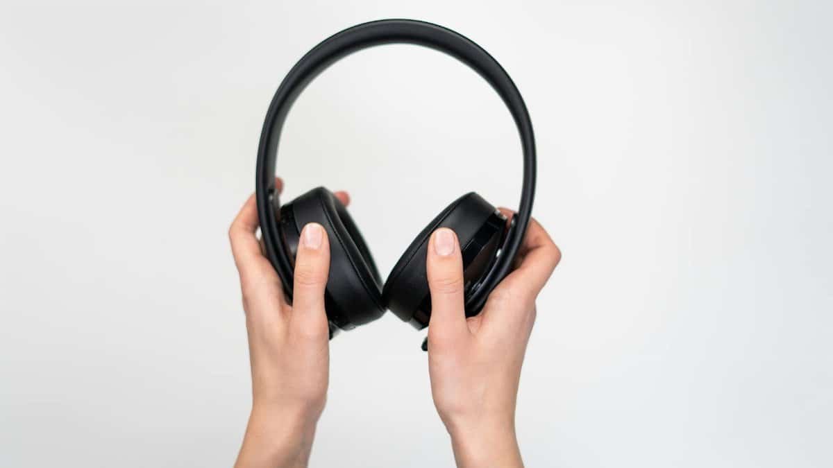 Close-up of hands holding black over-ear headphones on a white background.