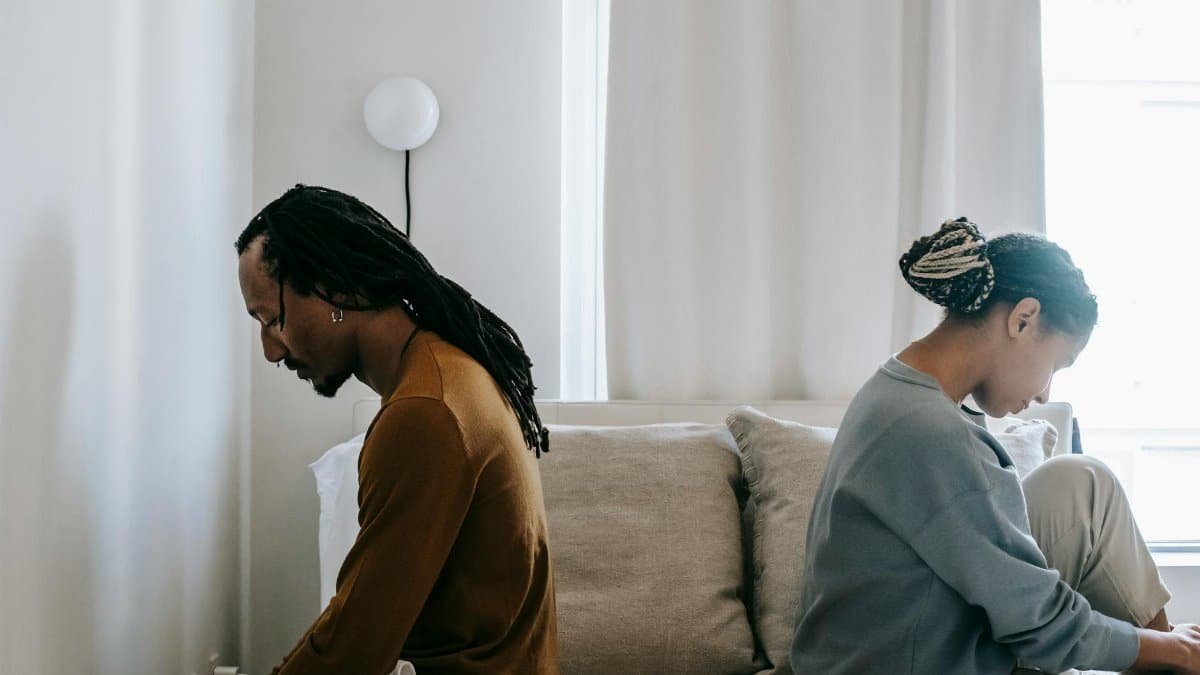 Side view unhappy sorrowful African American couple sitting on bed back to back after having argument