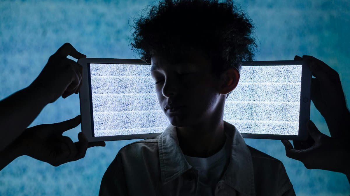 A teenager stands with eyes closed between two tablets showing digital noise, symbolizing information overload.