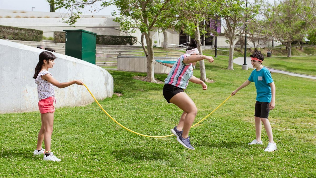 Three children playing with a skipping rope in a sunny park, showcasing outdoor fun and exercise.
