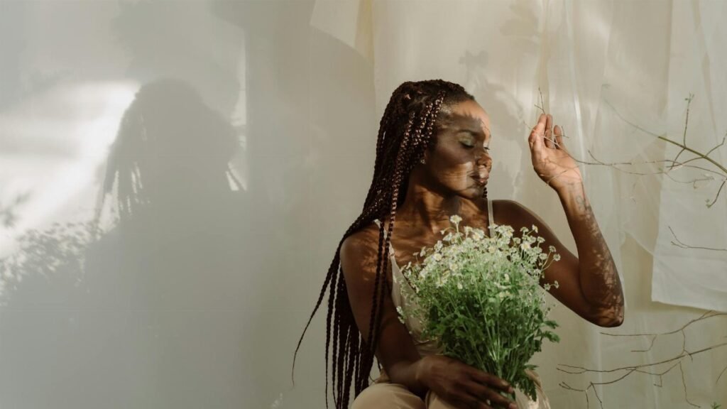 A serene portrait of a woman with braids holding chamomile flowers, bathed in gentle lighting.