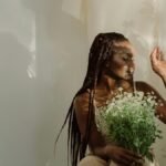 A serene portrait of a woman with braids holding chamomile flowers, bathed in gentle lighting.