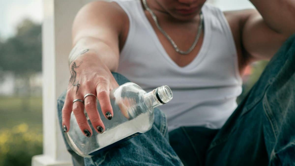 Pensive young man with tattoos holding an empty bottle outdoors during the day.