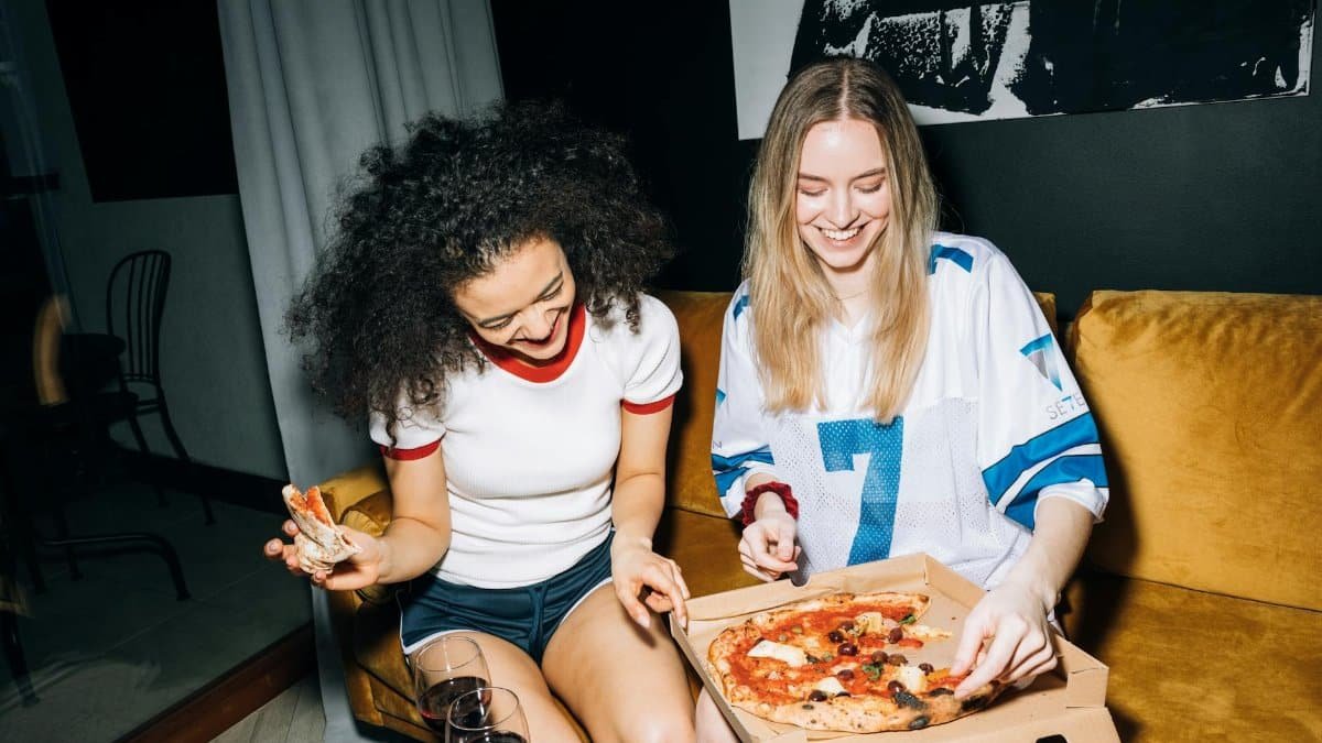 Two young women having fun and eating pizza on a cozy night in, capturing friendship and joy.