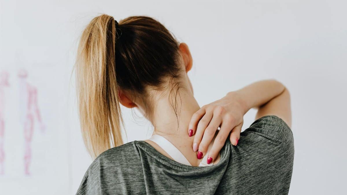 A woman in casual clothing holds her neck, indicating pain or discomfort.