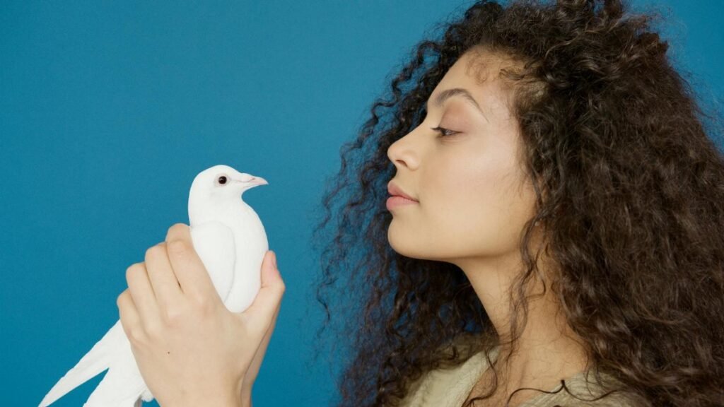 A woman with curly hair holds a white dove against a blue background, conveying peace.