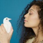 A woman with curly hair holds a white dove against a blue background, conveying peace.