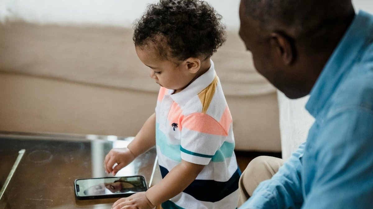 A father watches as his young son engages in a video call, reflecting modern family bonding indoors.