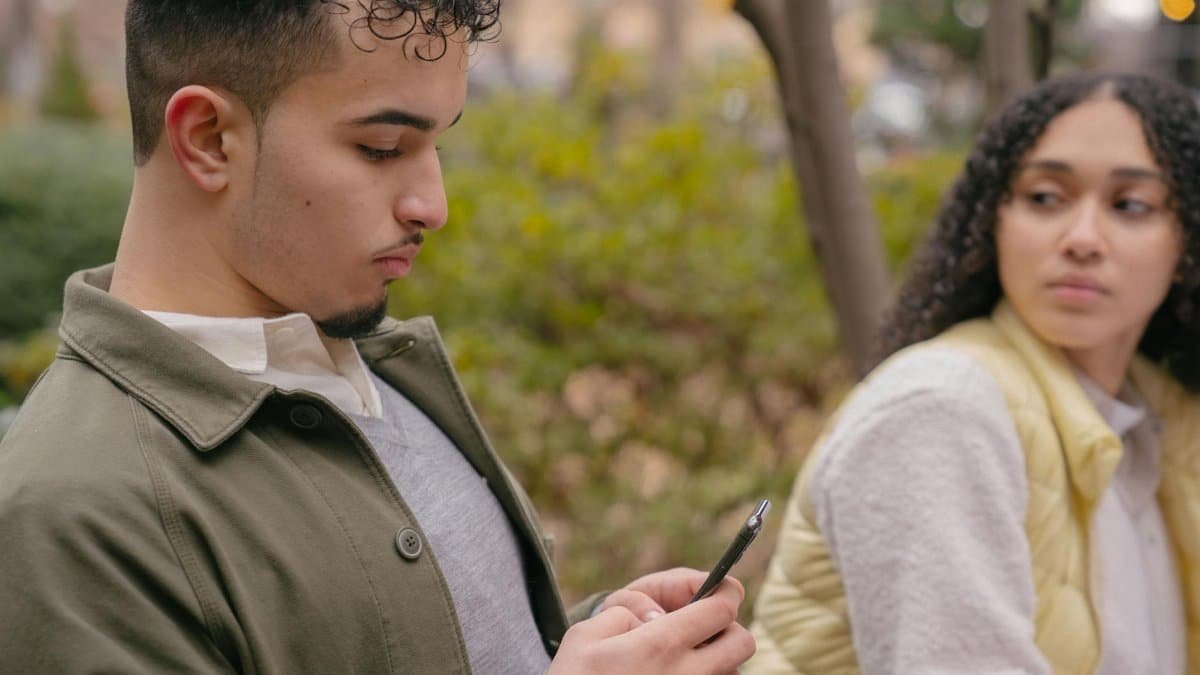 A young couple sitting outdoors with a smartphone, capturing casual moments and emotions.