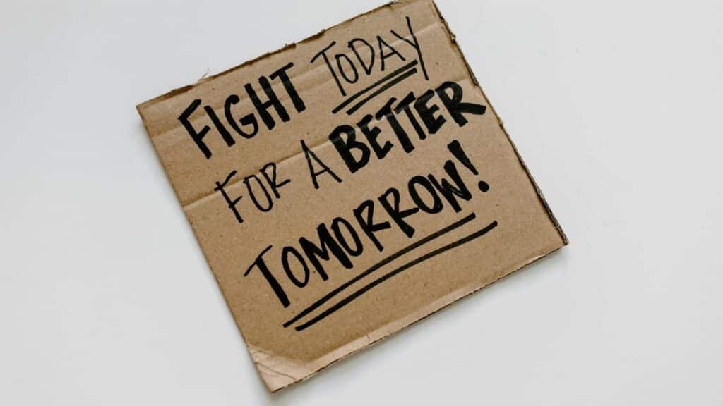 Cardboard sign with 'Fight today for a better tomorrow!' message on a white background.