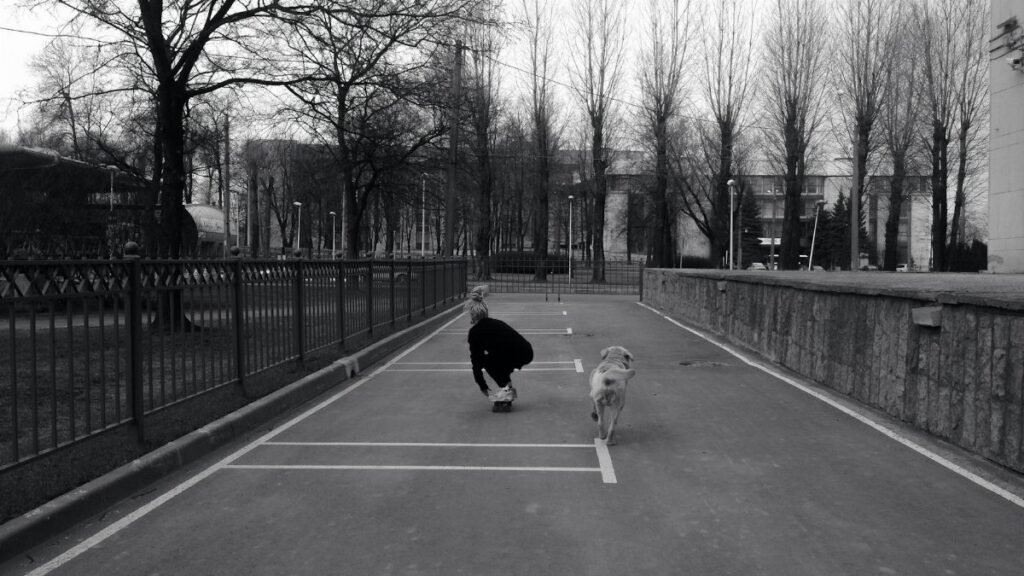 A person skateboards with a dog on an urban street, captured in black and white.