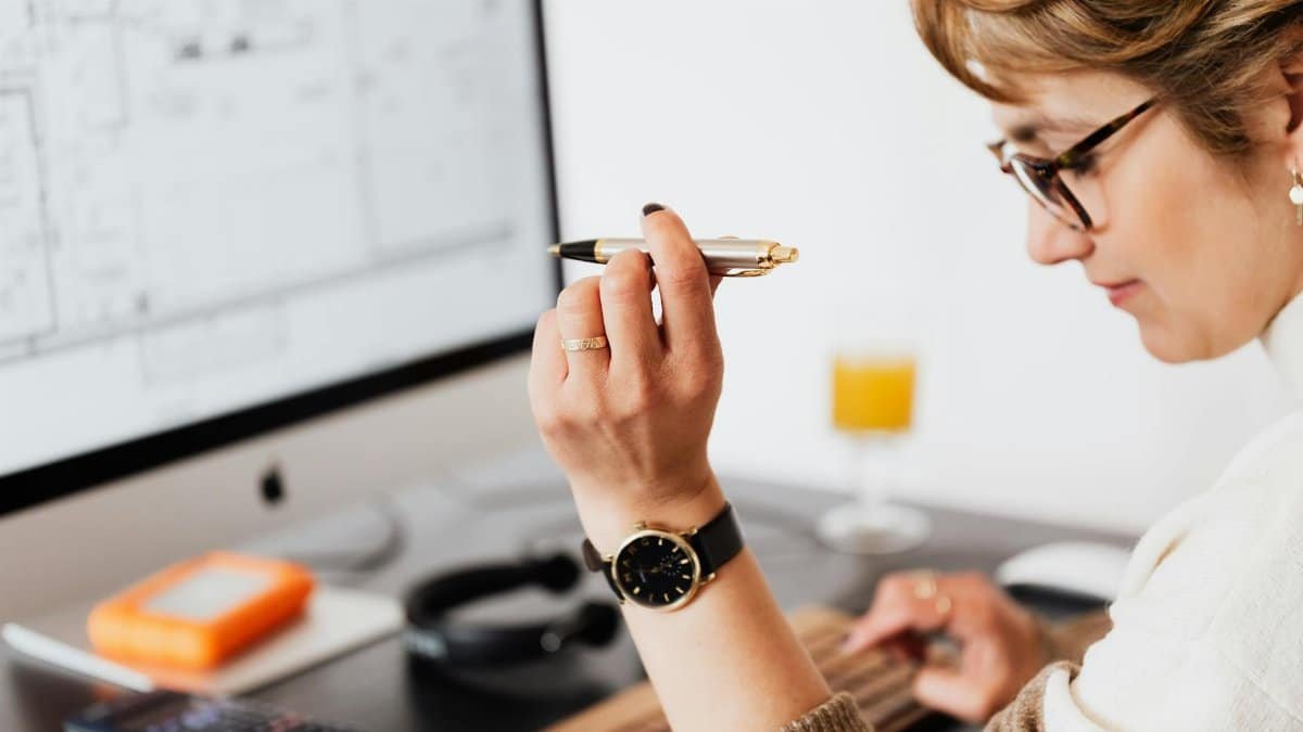 Side view of crop focused businesswoman in eyeglasses with pen in hand making report of financial results while working on computer