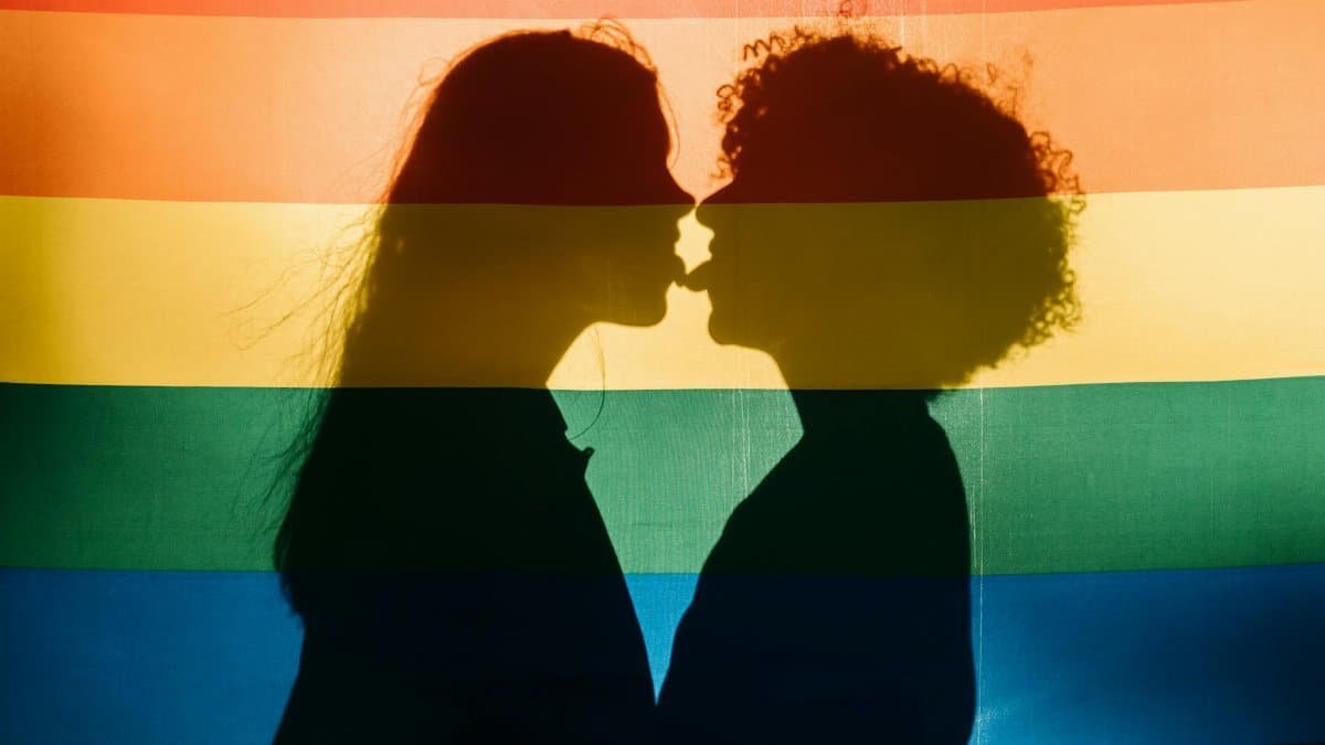 Silhouette of couples showing affection behind a colorful LGBT rainbow flag, capturing love and pride.