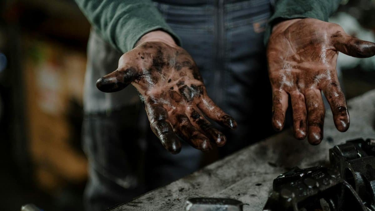 Close-up of a mechanic's dirty hands in a garage workspace with grease and spare parts.