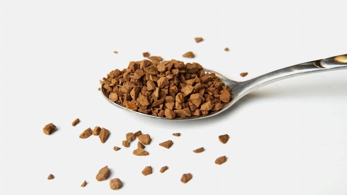Close-up of instant coffee granules on a silver spoon against a white background.