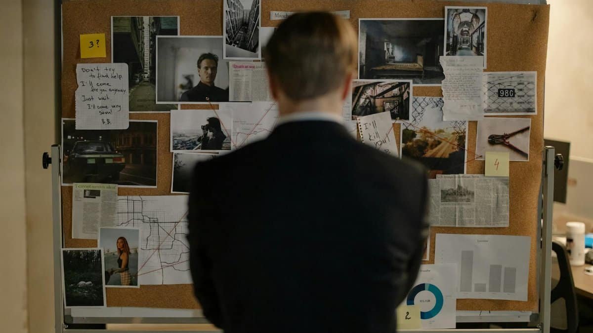 Detective examining clues on a bulletin board filled with photos and notes.