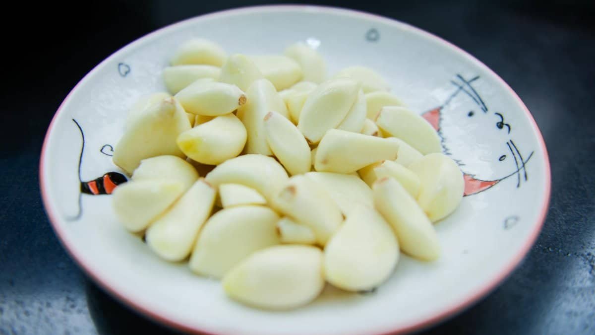 A close-up photo of peeled garlic cloves arranged on a decorative plate, highlighting their freshness.