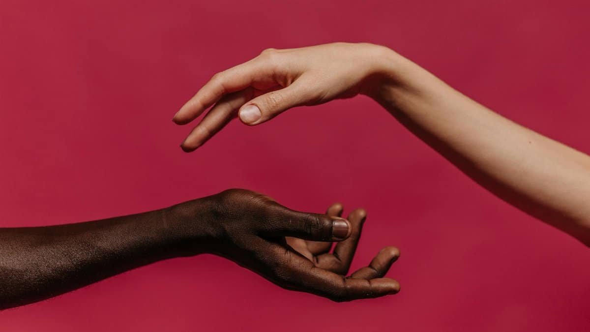 Two hands reaching towards each other against a vibrant pink background, symbolizing connection and diversity.