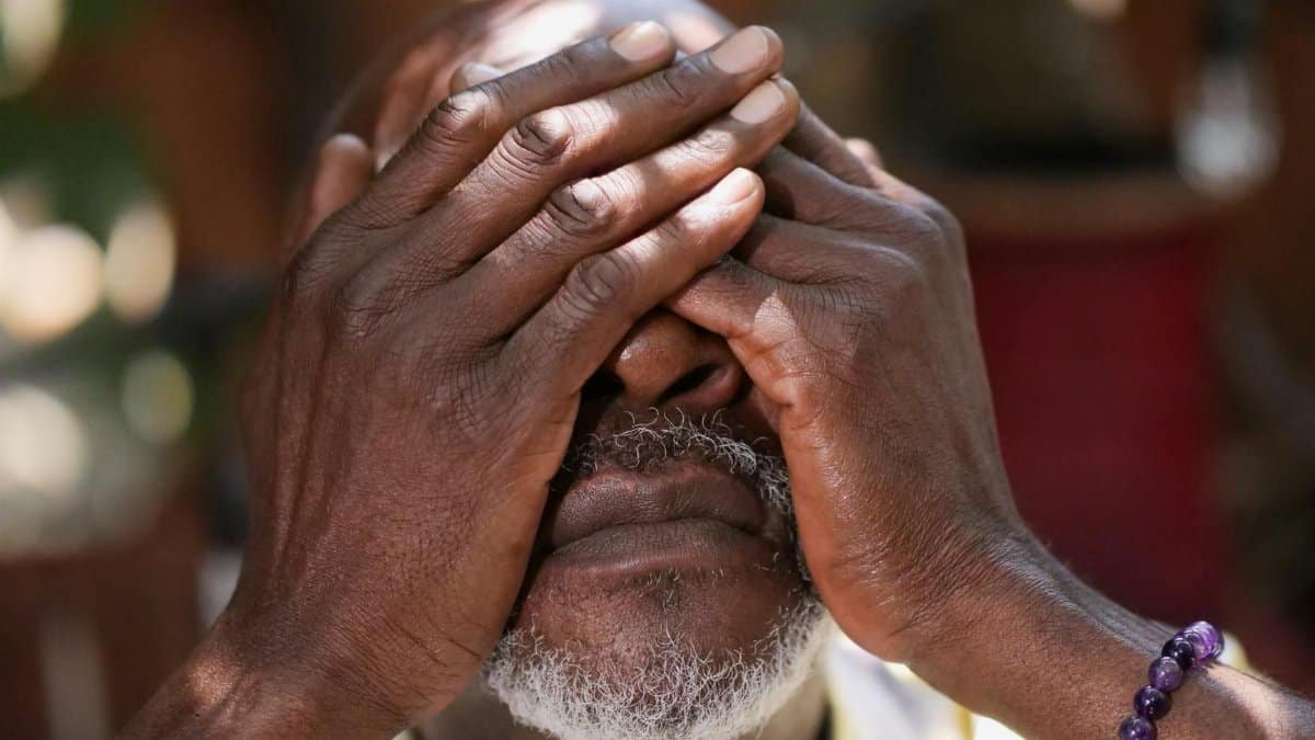 Close-up of an elderly man with a beard covering his face with his hands outdoors.