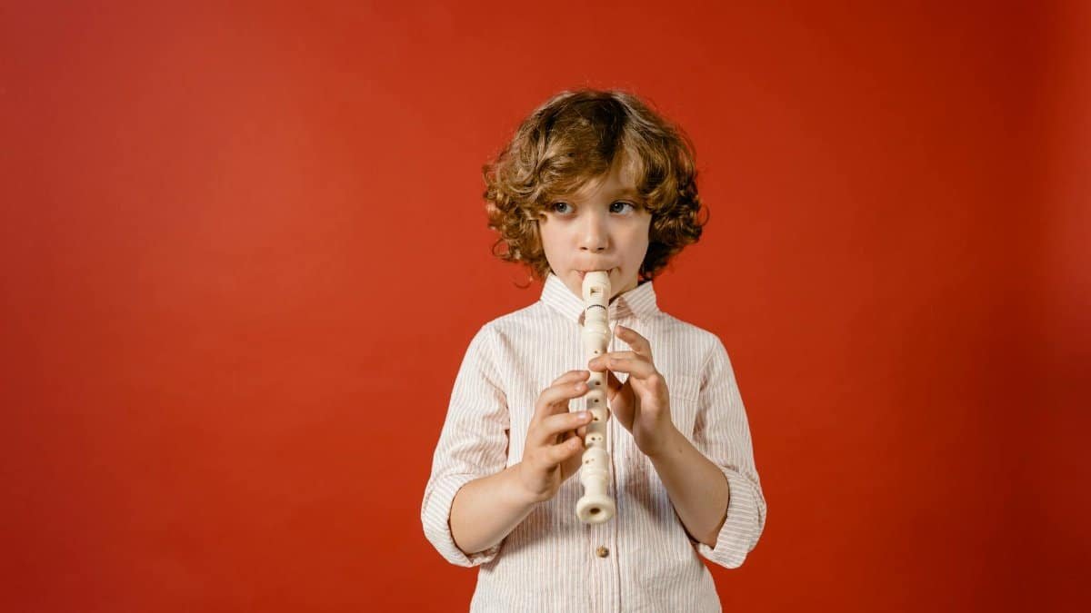 A young boy playing the flute with a red background, highlighting musical talent and focus.