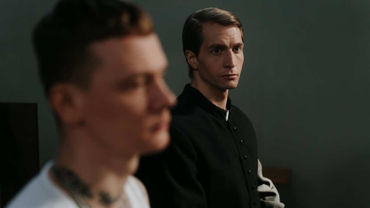 Two men, one in focus, sit thoughtfully indoors, highlighting contemplation.