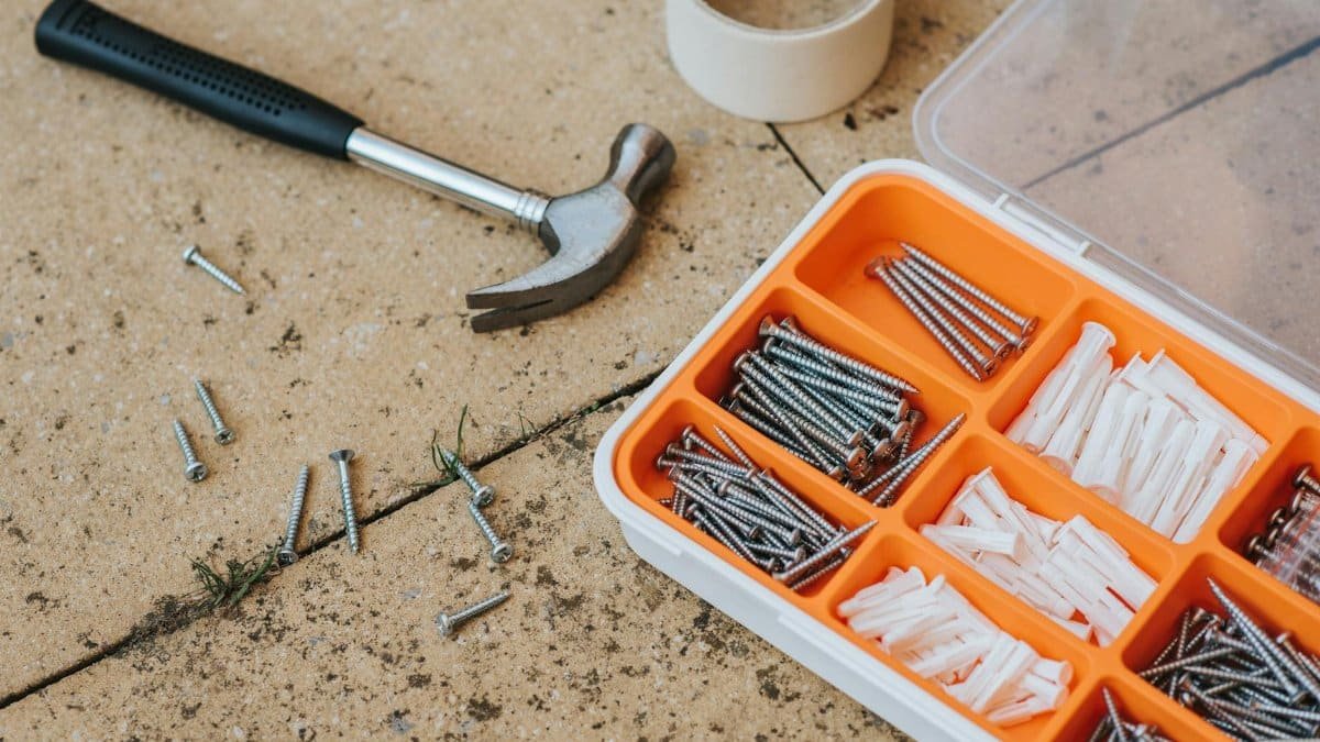 Overhead view of a toolkit with a hammer, screws, and anchors on a concrete surface.