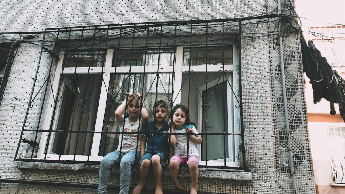 Three children sitting in front of window bars in a residential area of Istanbul.