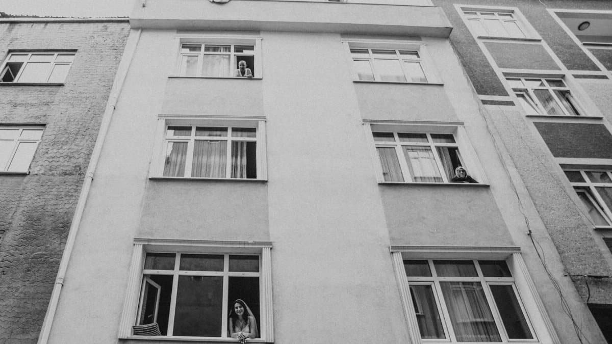 Black and white photo of people looking out from an apartment building windows.