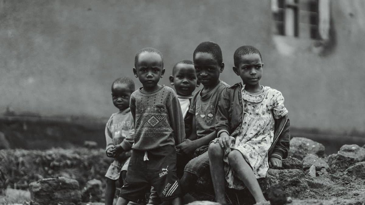 A group of children sitting beside an old building, captured in black and white