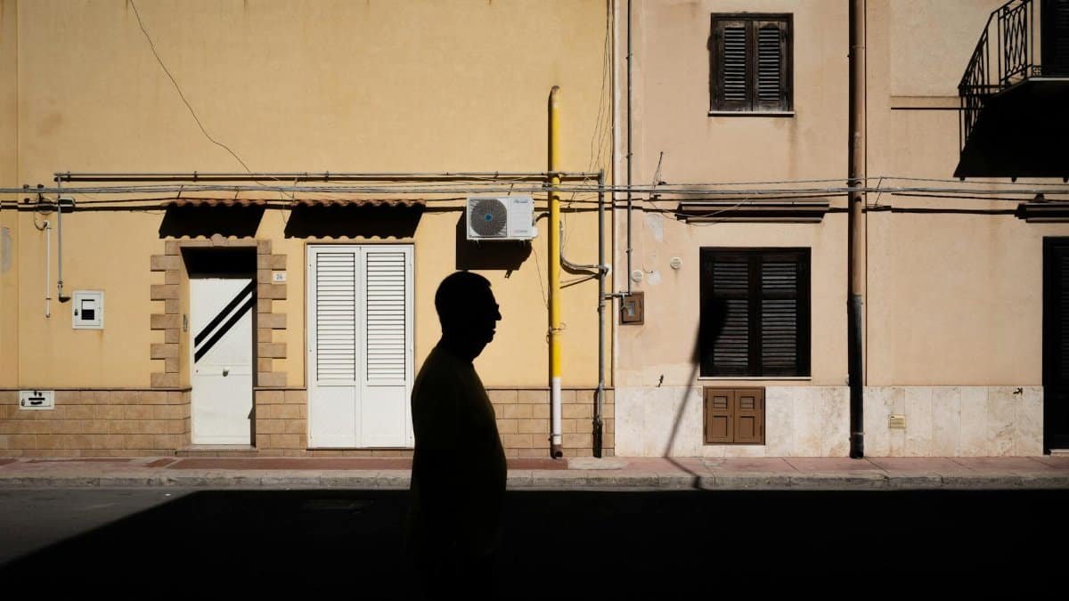 A man in silhouette walks past a sunlit building, casting a shadow on the urban street.