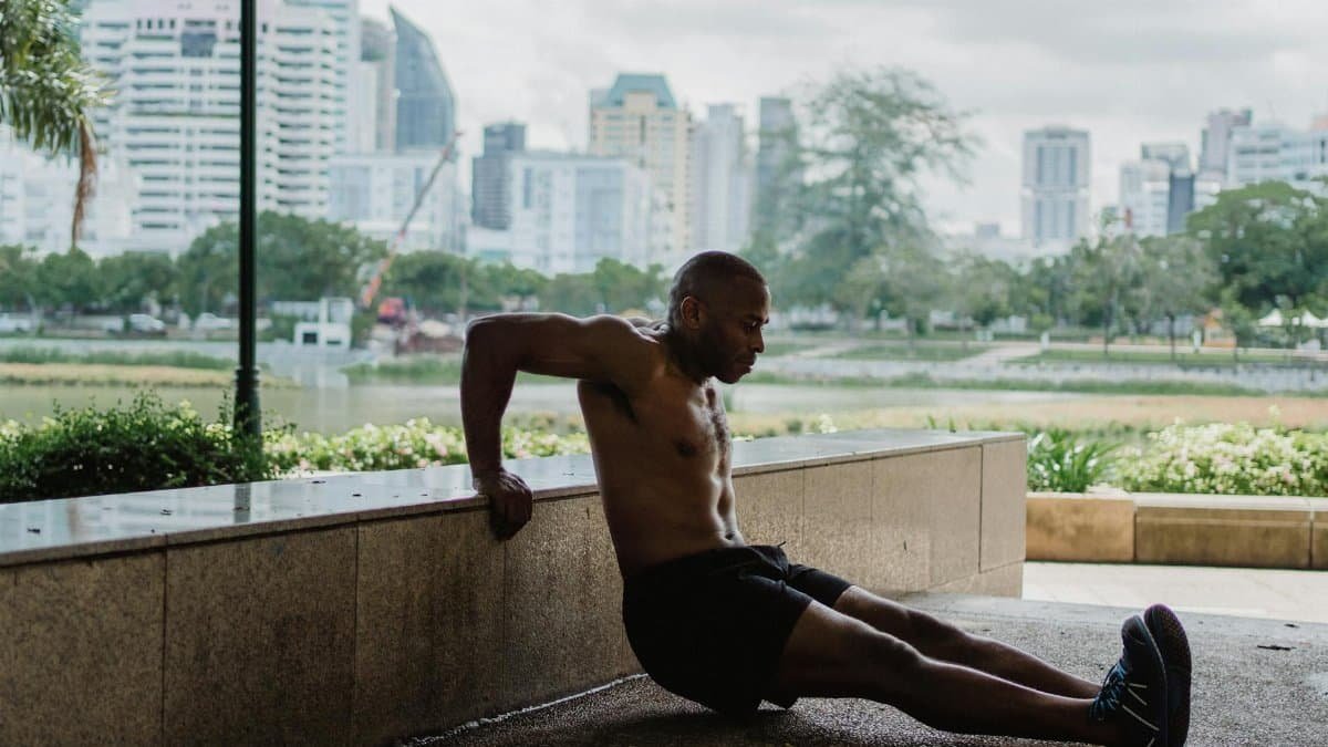 A fit man performs tricep dips in an urban park with a city skyline backdrop, embracing strength and wellness.