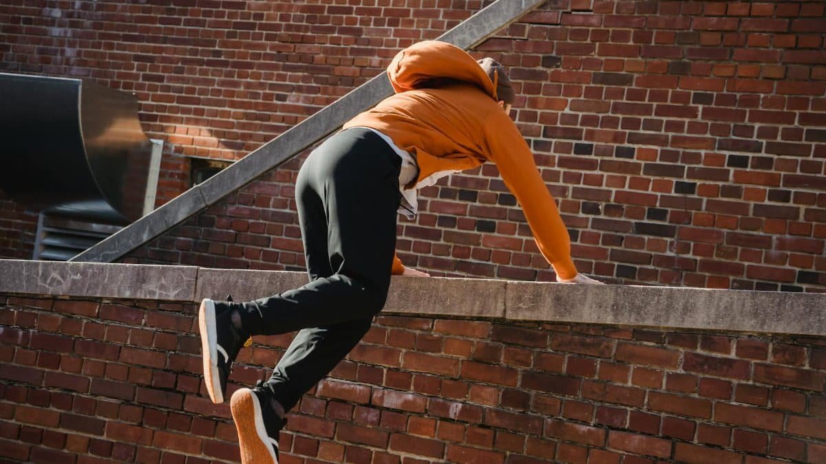 Back view anonymous male tracer in casual wear performing tricks while practicing parkour on brick building
