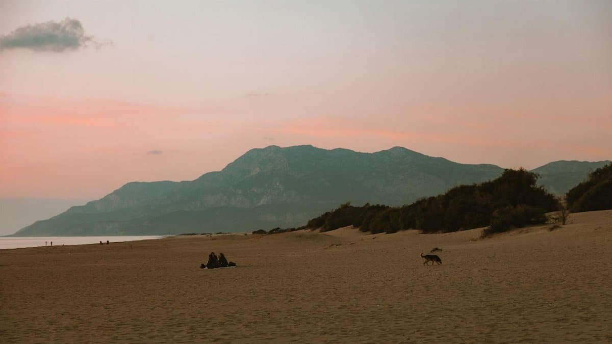 A serene beach landscape at sunset with mountains and a calm atmosphere.