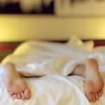 A person relaxing on a bed with feet under white sheets, conveying serenity.
