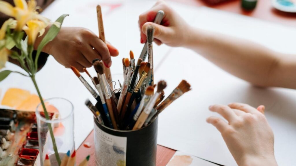 Hands reaching for paintbrushes in an artistic indoor setting.