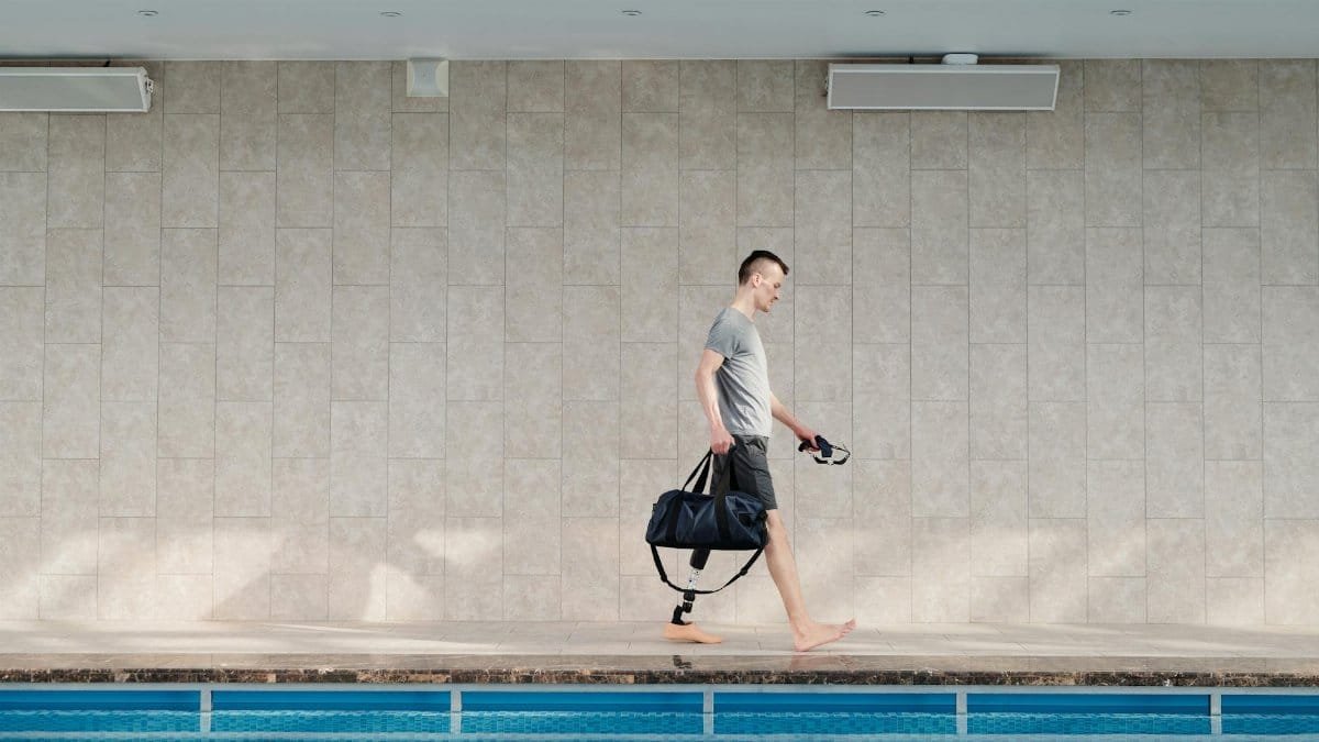 A determined amputee with a prosthetic leg walking confidently by a swimming pool indoors.