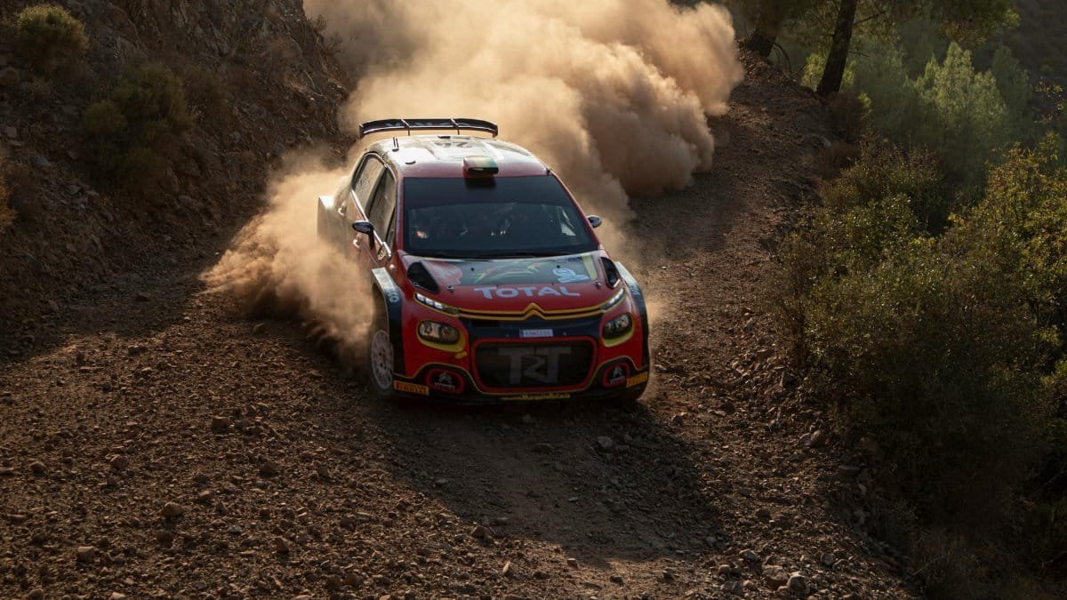 A rally car speeds through a dirt road, kicking up dust in an intense endurance race.