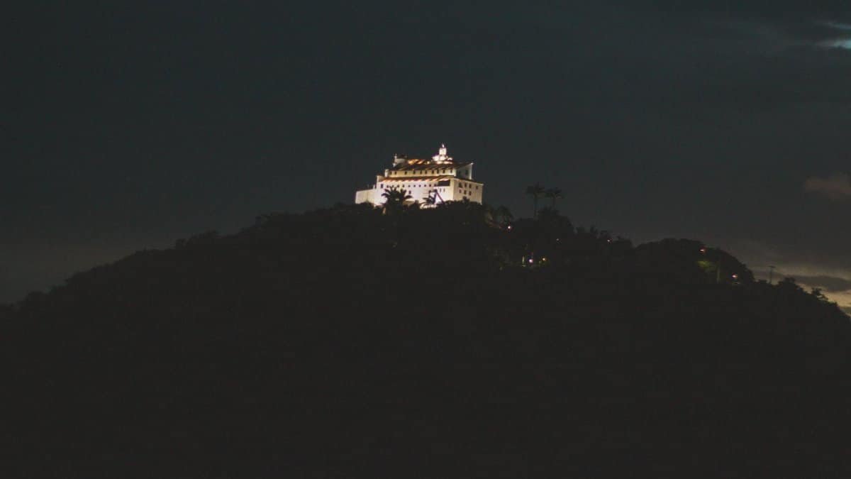 A serene view of a lit building atop a hill under the night sky, radiating mystique.